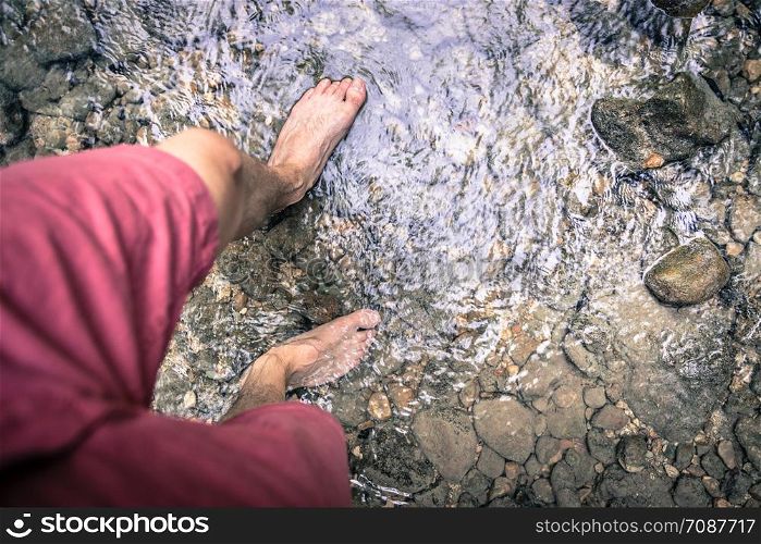 Cut out of male barefoot feet with red trousers walking in a shallow river