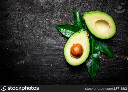 Cut ripe avocado with leaves. On a black background. High quality photo. Cut ripe avocado with leaves.