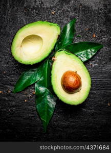 Cut ripe avocado with leaves. On a black background. High quality photo. Cut ripe avocado with leaves.