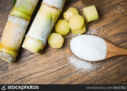 Cut sugar cane piece and white sugar on wooden spoon background top view