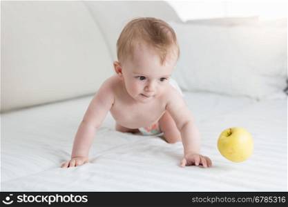 Cute 10 months old baby boy playing with yellow apple on bed