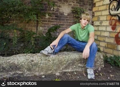 Cute 15 year old boy sitting outside by brick wall.