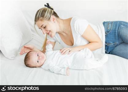 Cute 3 months old baby boy lying on bed with young smiling mother