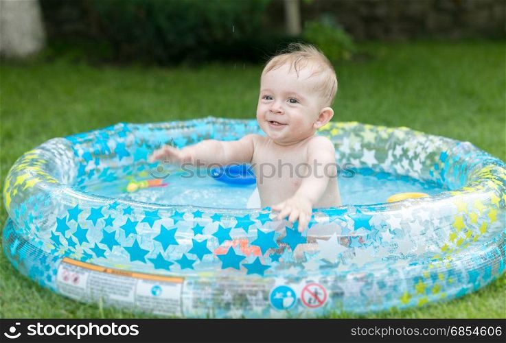 Cute 9 months old baby boy having fun in inflatable swimming pool