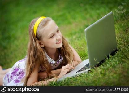 Cute 9 Years Girl Lying Down on Front on the Green Grass and Looking at the Laptop
