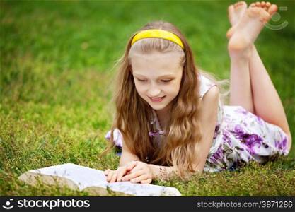 Cute 9 Years Girl Lying Down on Front on the Green Grass and Reading a Book