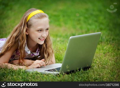 Cute 9 Years Girl Lying Down on Front on the Green Grass and Looking at the Laptop