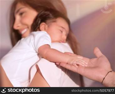Cute adorable newborn daughter sleeping on mothers shoulder and father with tenderness holding her tiny hand, love concept