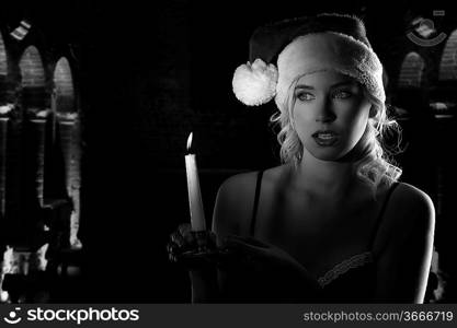 cute and attractive young woman with nightgown ant a christmas hat looking in the dark with a candle