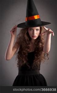 cute and pretty girl with long curls posing for halloween wearing a huge black and orange hat