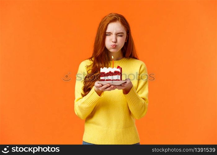 Cute and silly, lovely redhead b-day girl close eyes, holding birthday piece cake, pouting as blow out candle to make wish, want dream come true, close eyes, celebrate with friends, orange background.. Cute and silly, lovely redhead b-day girl close eyes, holding birthday piece cake, pouting as blow out candle to make wish, want dream come true, close eyes, celebrate with friends, orange background
