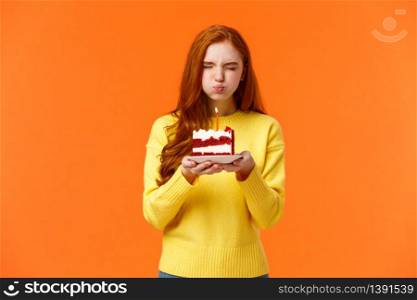 Cute and silly, lovely redhead b-day girl close eyes, holding birthday piece cake, pouting as blow out candle to make wish, want dream come true, close eyes, celebrate with friends, orange background.. Cute and silly, lovely redhead b-day girl close eyes, holding birthday piece cake, pouting as blow out candle to make wish, want dream come true, close eyes, celebrate with friends, orange background