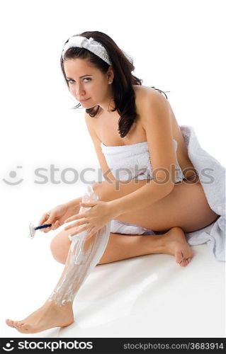cute and young brunette dressing white towel shaving her legs with foam and making face