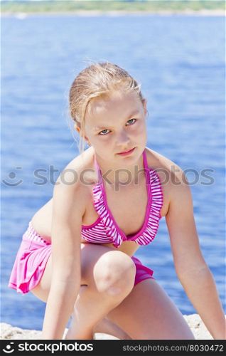 Cute angry girl on the riverbank in pink swimsuit