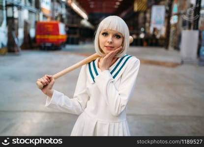 Cute anime style blonde girl with baseball bat. Cosplay fashion, asian culture, doll in dress, sexy woman with makeup in the factory shop