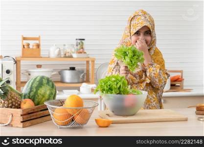Cute Arab muslim kid girl wearing hijab do not like to eat and smell of salad vegetables while using hand cover her nose in kitchen at home. Child do not like smell of green vegetables concept