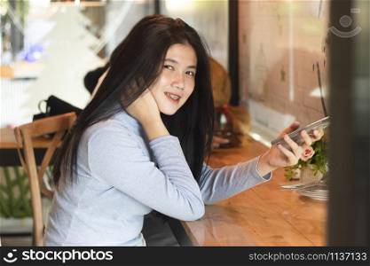 Cute asian girl holding smartphone in cafe
