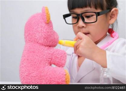 Cute Asian little girl playing doctor role game is giving injection to her sick teddy bear friend. Homeschool children’s play and learning.