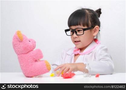Cute Asian little girl playing doctor role game is giving injection to her sick teddy bear friend. Homeschool children’s play and learning.