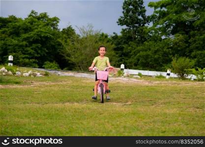 Cute Asian little girl riding a bicycle on the lawn on a hot summer day. Happy little girl riding a bicycle outdoors. Healthy Summer Activities for Kids