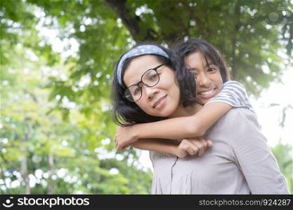 Cute Asian mother and daughter playing and giving ride on back together at park, Happy family concept