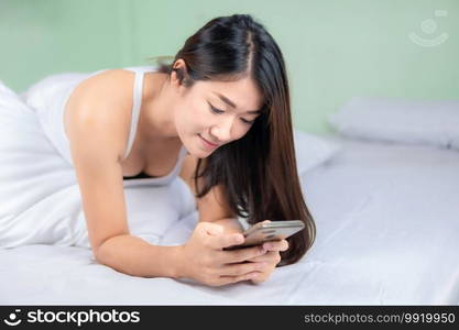 Cute asian woman use of mobile phone in bedroom and smile.