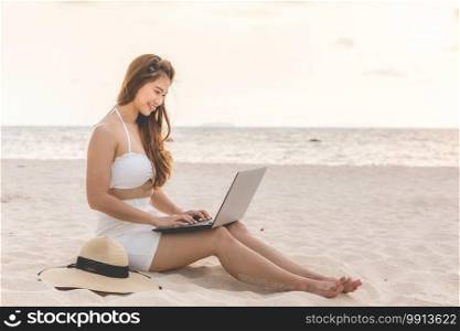 Cute Asian woman working with computer laptop on the tropical island beach with sunset feeling so happiness and comfortable,Summer Vacations and Freelance concept