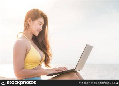 Cute Asian woman working with computer laptop on the tropical island beach with sunset feeling so happiness and comfortable,Summer Vacations and Freelance concept