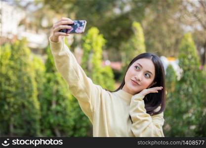 Cute Asian women are using their phones to take selfies and smile happy in the garden at home.