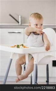 cute baby boy highchair eating vegetables kitchen