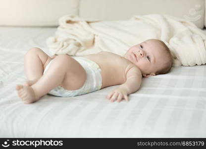 Cute baby boy in diapers lying on bed