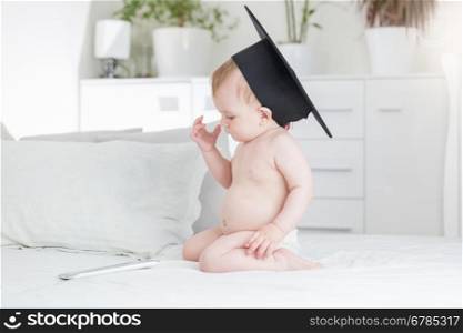 Cute baby boy in graduation cap looking at digital tablet