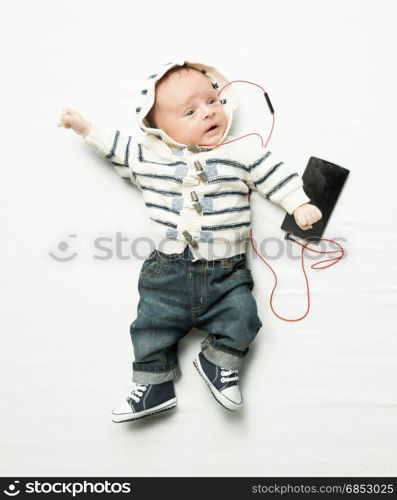 Cute baby boy listening to music on phone with earphones