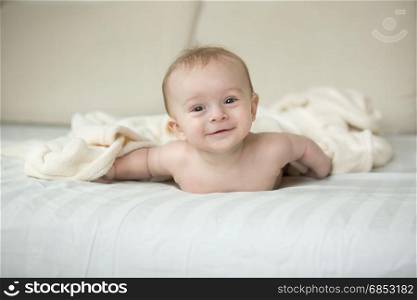 Cute baby boy lying on bed under big white blanket