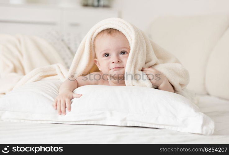 Cute baby boy lying on bed under towel after bathing