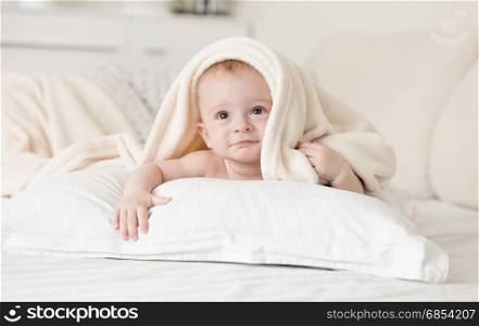 Cute baby boy lying on bed under towel after bathing