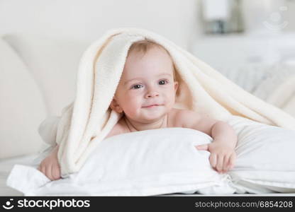 Cute baby boy lying under white blanket on bed