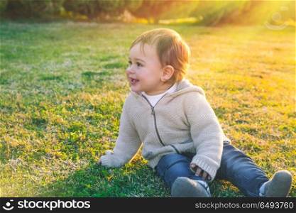 Cute baby boy outdoors, sweet little child sitting on fresh green grass field in bright sunny day, enjoying first spring days, happy carefree childhood. Cute baby boy outdoors