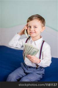 Cute baby boy playing with a lot of money like talking on telephone, american hundred dollars cash. American one hundred dollars in cash. Portrait boy with banknotes.. Cute baby boy playing with a lot of money like talking on telephone, american hundred dollars cash. American one hundred dollars in cash.