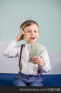 Cute baby boy playing with a lot of money like talking on telephone, american hundred dollars cash. American one hundred dollars in cash. Portrait boy with banknotes.. Cute baby boy playing with a lot of money like talking on telephone, american hundred dollars cash. American one hundred dollars in cash.