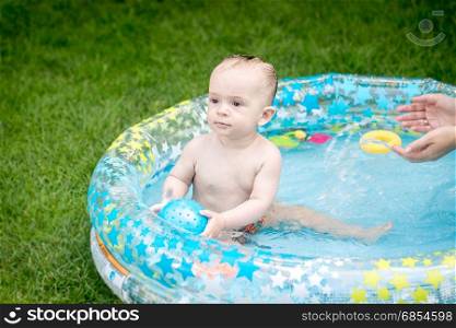 Cute baby boy playing with ball in the swimming