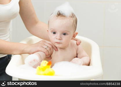 Cute baby boy playing with yellow rubber duck in bath