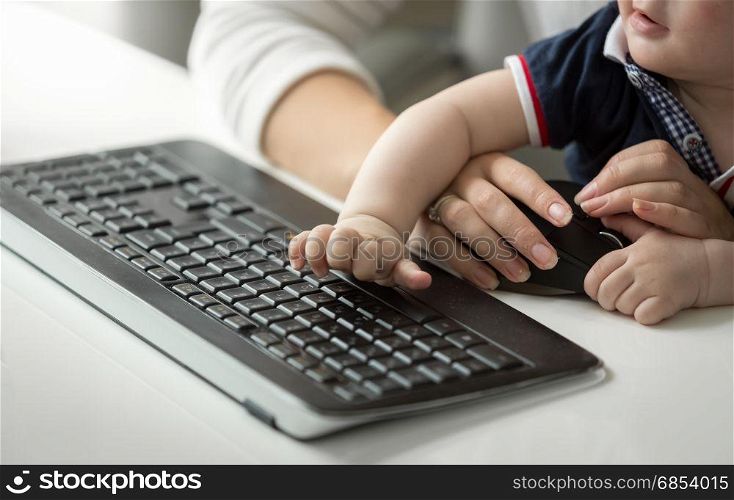 Cute baby boy sitting on mothers lap while she is working at computer