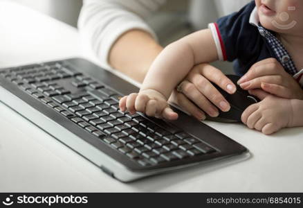 Cute baby boy sitting on mothers lap while she is working at computer