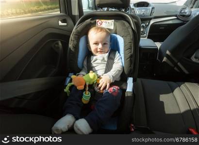 Cute baby boy sitting with toys in child car seat