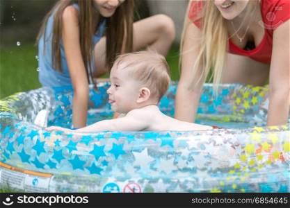 Cute baby boy swimming in outdoor pool with mother and sister