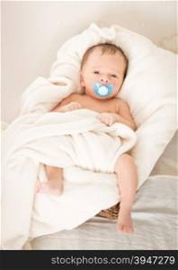 Cute baby boy with soother lying in wicker basket