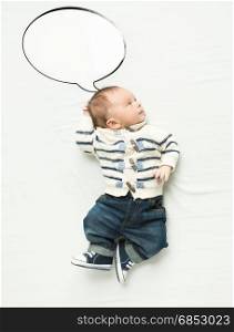 Cute baby boy with speech bubble lying on bed