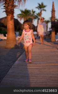 cute baby girl and mother walking togeter from the beach at beautiful sunset in background