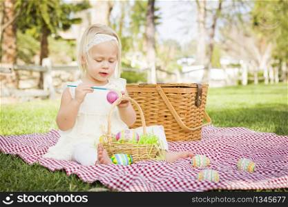 Cute Baby Girl Enjoys Coloring Her Easter Eggs on Picnic Blanket in the Grass.